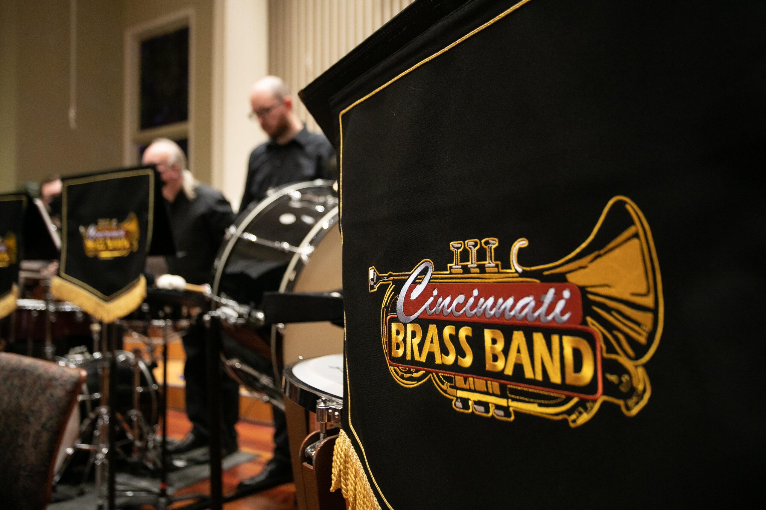 A music stand banner with the Cincinnati Brass band logo in the foreground and some of our percussion players in the background